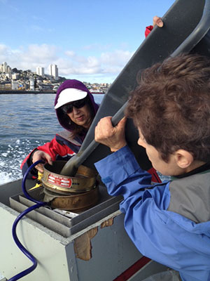 San Francisco Public Utilities Commission (SFPUC) biologist Patricia McGregor and USGS micropaleontologist Mary McGann process sediment samples from San Francisco Bay onboard the SFPUC's motor vessel Rincon Point. The San Francisco skyline is visible in the background.