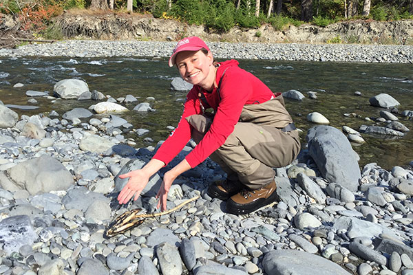 Photograph of researcher Amy East, with her discovery of a salmon carcass on the banks of the upper Elwha River.