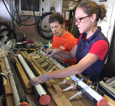 Photograph of scientists sampling pore fluids from sediment cores collected aboard the ship offshore of southeast Alaska. Photo by Jamie Conrad, USGS.